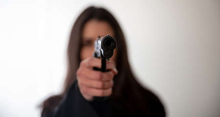 Woman holding a gun in hand pointing at camera. Female secret police agent, killer or spy dark long hair, copy space. Selective focusの写真素材