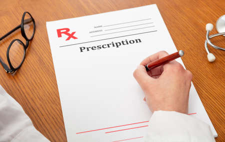 Medical prescription. Woman doctor holding a pen, close up above view, wooden office table background. Female hand over empty document, copy spaceの写真素材