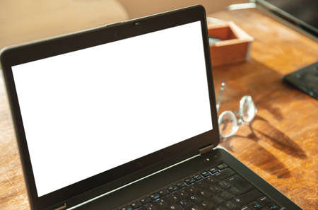 Computer screen mockup. Laptop open with white blank screen on a wooden desk, office background,...