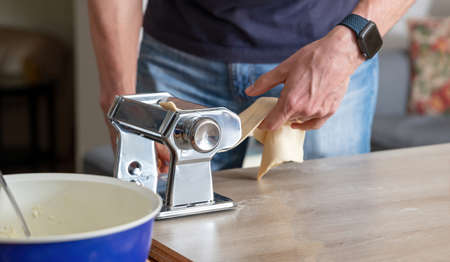 Pasta maker machine. Fresh pasta homemade preparation. Male hand making dough phylo close up view