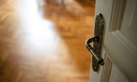 Door open close up view. Retro doorknob on white vintage wooden door, blur empty wood floor parquet, classy house room interiorの写真素材