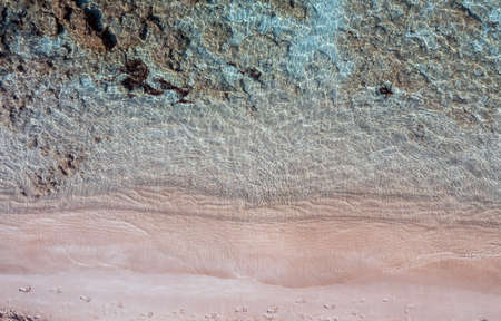 Sandy beach, turquoise blue color sea aerial top view. Footprints on wet pink sand. Clear...