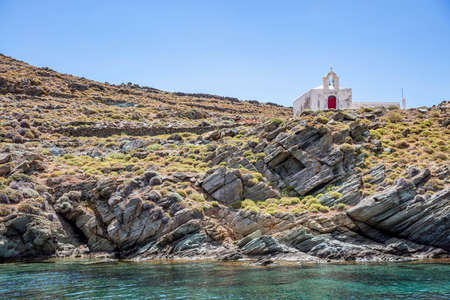 Greek small Church on the rocky hill, over turqoise sea water, blue sky background, sunny summer day. Agios Ioannis chapel, Kythnos island, Greeceの写真素材