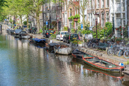 Boats moored on the canal water. Amsterdam Netherlands. Parked bicycles and cars on the street, traditional brick facade houses, copy spaceの写真素材
