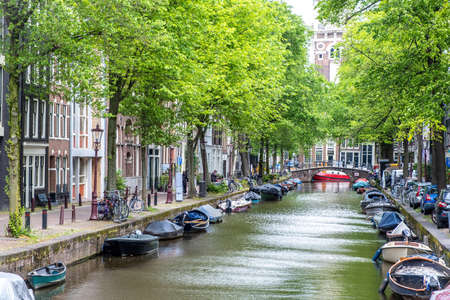 Boats moored along the canal, Amsterdam. Parked bicycles and cars on the street, traditional ...
