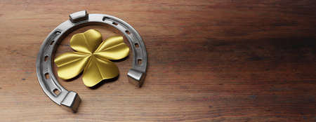 Silver shiny horseshoe with golden four leaf clover on wooden background. St Patrick Day, March 17, lucky horseshoe and shamrock. Copy space, banner. 3d illustrationの写真素材
