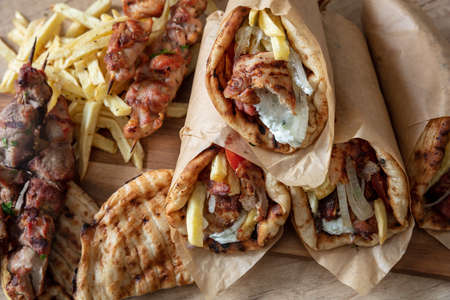 Greek traditional street food, gyro sliced meat, souvlaki skewer. Pita bread, tzatziki yogurt, potato tomato and onion on wooden table, top viewの写真素材