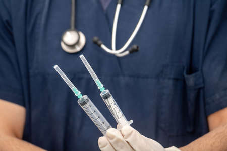 Doctor in medical uniform holds, in hand with disposable glove, empty syringe. Blur physician with the stethoscope around his neck. Healthcare concept.の写真素材