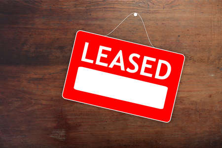 LEASED red sign with white word and empty space for text, advertising template. Label for hired real estate on old wood surface, agreement with agent. Copy spaceの写真素材