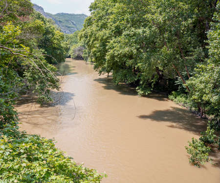 Greece. Pineios River in Vale of Tempi, Thessaly.  River brown water flowing, large green trees on...