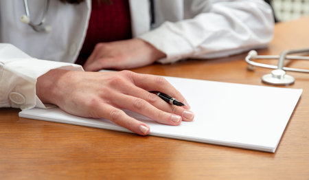 Woman doctor holding a pen on a blank white paper, close up view, wooden office table background. Female hand over empty documentの写真素材