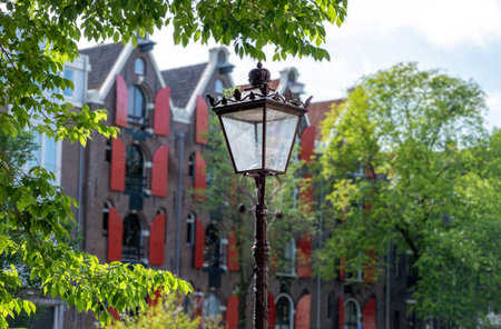 Antique metal and glass lantern, ornate streetlight between trees in Amsterdam city. Blur iconic canal house, Holland Netherlands.の写真素材