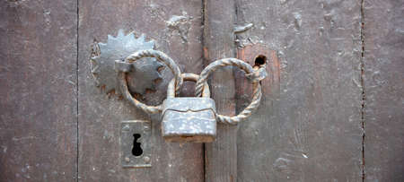 Old vintage wooden door locked with rusty padlock on metal double handle. Close up view of keyhole...