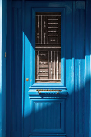 Wooden closed blue door background. Traditional Greek island construction, vintage entrance with grid on glass, metal handle, sunny day. Verticalの写真素材
