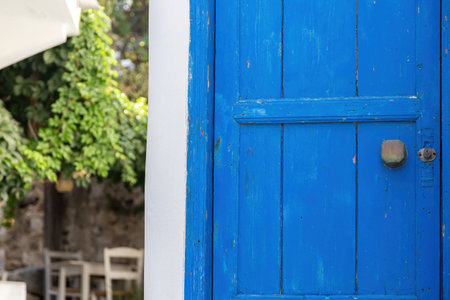 Wooden closed blue old door with rusty handle and keyhole. Greek island vintage entrance, blur traditional cafe, table chairs, plants background.の写真素材