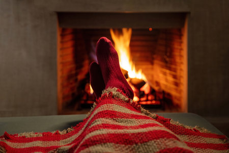 Man covering with blanket enjoys the calmness next to burning fireplace. Winter holiday fireside and flames background, warm home interior.の写真素材
