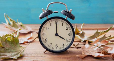 Daylight Saving Time, Fall Back. Black alarm clock and autumn leaves on wooden table