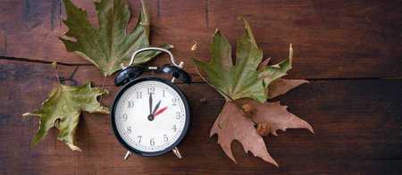 Fall Back, Daylight Saving Time. One hour back on yellow clock and autumn leaves on wooden background, top viewの写真素材