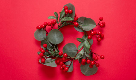 Christmas decoration. Cotoneaster wreath Xmas garland plant with berries on red background. Greeting card template copy space.の写真素材