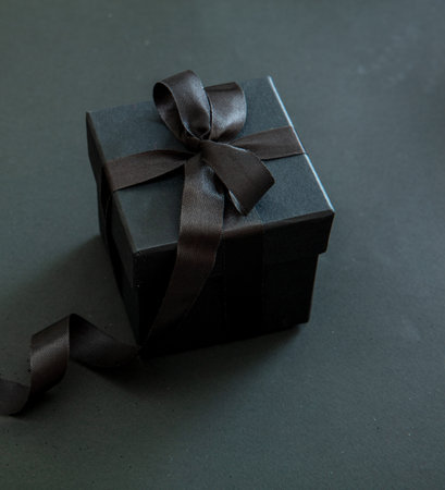 Black Friday Sale. Gift box with black ribbon isolated on black, close up view. Christmas presents...