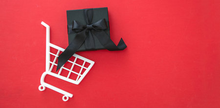 Black Friday Sale. Gift box in a Shopping Cart, red background, copy space. E commerce, online shop sales conceptの写真素材