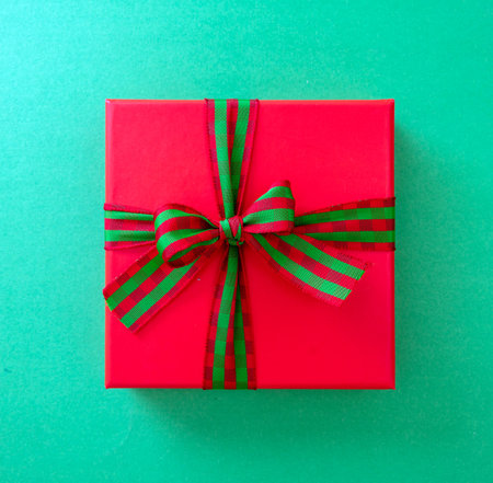 Xmas Anniversary Valentine Day Birthday present. One red gift box wrapped with luxury striped red green ribbon on green background, top view.の写真素材