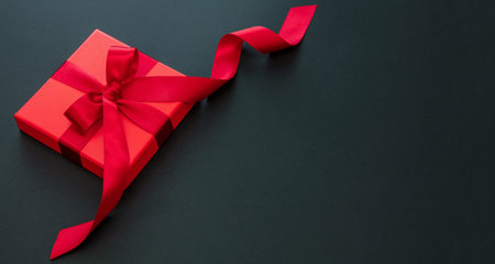 Black Friday sales, Birthday Valentines day. Red gift box luxury passion red satin ribbon on black background, top view, copy space.の写真素材