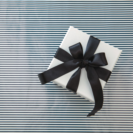 Birthday Anniversary Xmas Valentine Day present. One white gift box wrapped with luxury black satin ribbon on striped background, top view.の写真素材