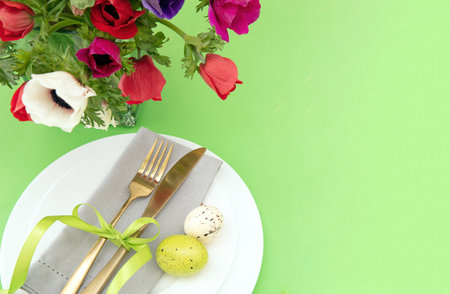 Easter table setting, Spring flowers and eggs decoration, napkin and golden cutlery on white plates, pastel green background, copy spaceの写真素材