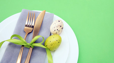 Easter table setting, Easter eggs decoration, napkin and golden cutlery on white plates, pastel...