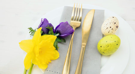 Easter table setting, Easter eggs, fresh Spring flowers decoration, napkin and golden cutlery on...