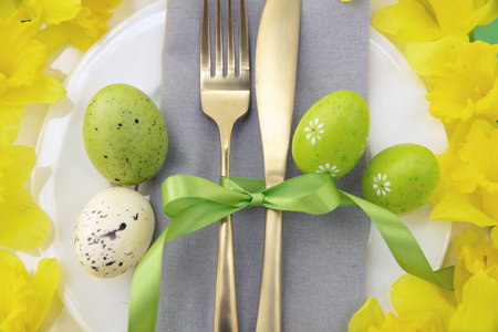 Easter table setting, Yellow Spring flowers and eggs decoration, napkin and golden cutlery on white...
