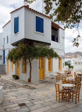 Greece. Tinos island Cyclades. Outdoors traditional cafe with yellow windows at Pyrgos village. Empty chair and table on paved yardの写真素材