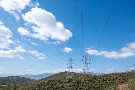 High voltage power lines and pylons on mountain, blue sky backgroundの写真素材