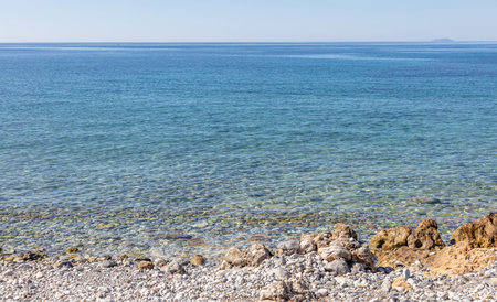 Rocky empty beach transparent calm sea water clear blue sky background. Greek rock coast, holiday resort, seascape, sunny day in nature.の写真素材
