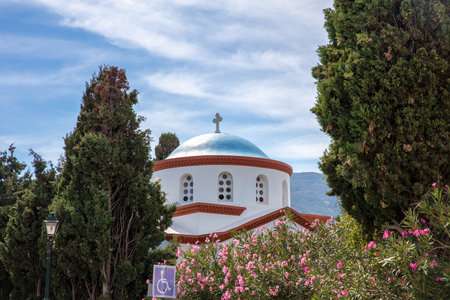 Andros island, Chora town, Cyclades destination Greece. White orthodox church cross arched window blue dome, view through tree, sky background.の写真素材