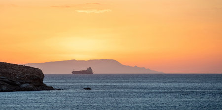 Sunset over Greek island as line ship leaves Cyclades. Sun colors the sky orange, yellow, hill...