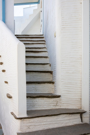 White painted old narrow stair background covered with stone between white wall. Small exterior step. Cyclades island architecture, Greece. Verticalの写真素材
