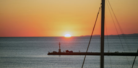 Sunset over Tinos island, Cyclades, Greece. View of ship mast, beacon silhouette golden sun colors the sky and dives into Aegean blue calm sea.の写真素材
