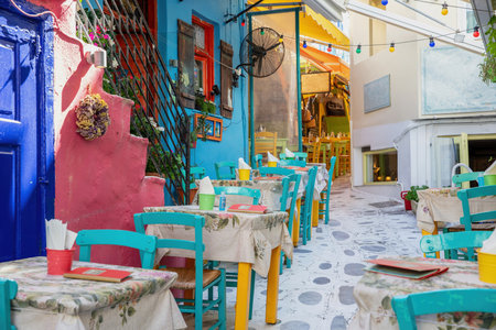 Outdoors traditional tavern restaurant in Greece, Tinos island Hora town Cyclades. Multicolor building, empty chair table, paved alley. Travelの写真素材
