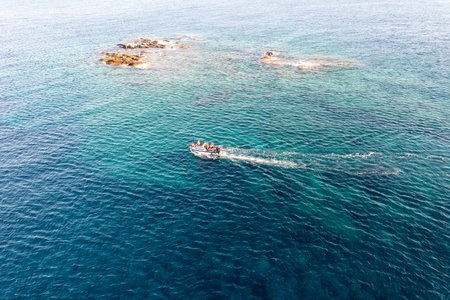 Speedboat sails in blue rippled Aegean Sea background next to rocky formation. Tinos island Cyclades, people enjoys summer vacation in Greece.の写真素材