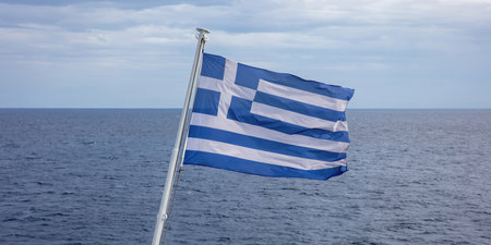 Greece sign symbol of leading shipping power in the world. Greek flag on flagpole waving over rippled sea water. Cloudy sky background.の写真素材