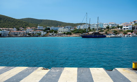 Greece, Megalochori, Milos, Miloi port, Agistri island. Traditional seaside building, tree on mountain, harbor with bollard, calm sea, blue sky.の写真素材