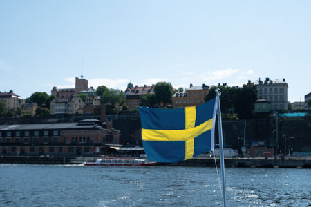 Sweden national flag waving, blur waterfront Stockholm buildings and blue sky background, sunny day,の写真素材