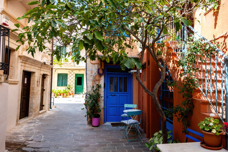 Chania Old Town, Crete island Greece. Traditional building, table, two chair and potted plant on narrow empty paved alley-yard, summer sunny day.の写真素材