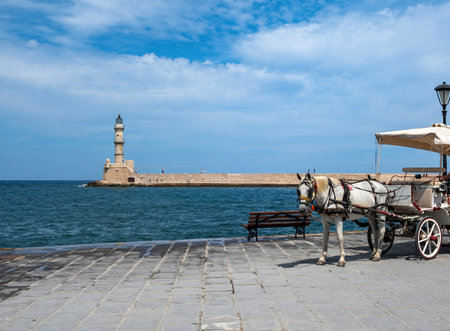 White horse drawn carriage and lighthouse at Venetian harbour , Old Town of Chania Crete, Greece. Traditional means of transport at seaside.の写真素材