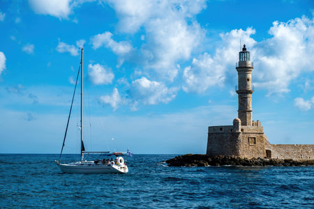 Lighthouse, beacon at Venetian harbour in Old Town of Chania Crete, Greece. Boat sailing in ripple sea water, summer vacation sunny day.の写真素材