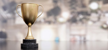 Gold steel trophy cup with dual handle on empty blur background. A reminder of a specific...
