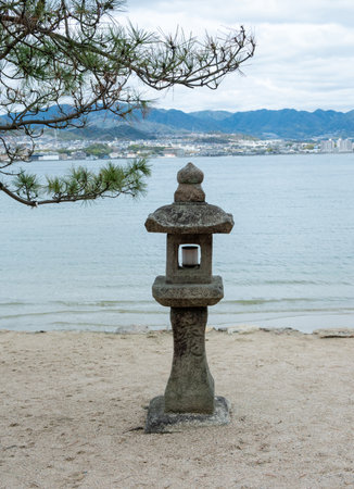 Japan, Miyajima island. Stone lantern and pine tree on sandy shore, cloudy skyの写真素材