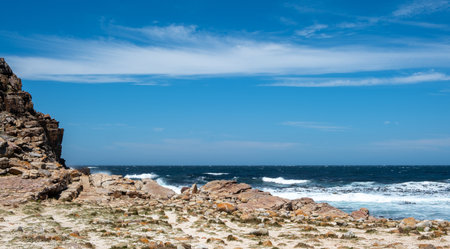 Ocean waves crashing on rocky coast, blue sky with scattered cloudsの写真素材